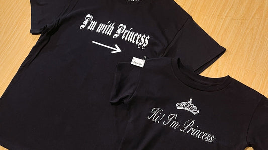 Two black t-shirts with text and graphics on a wooden surface