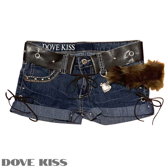 A pair of blue denim shorts featuring a wide black faux-leather belt with silver studs, lace-up side details, a dangling silver heart charm, and a brown faux-fur accent, shown on a white background with DOVE KISS branding.
